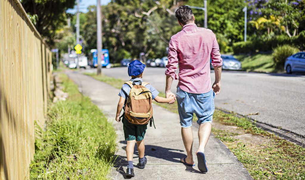 Rear view of an Australian aboriginal father taking his son to school, they are walking in the street holding hands.