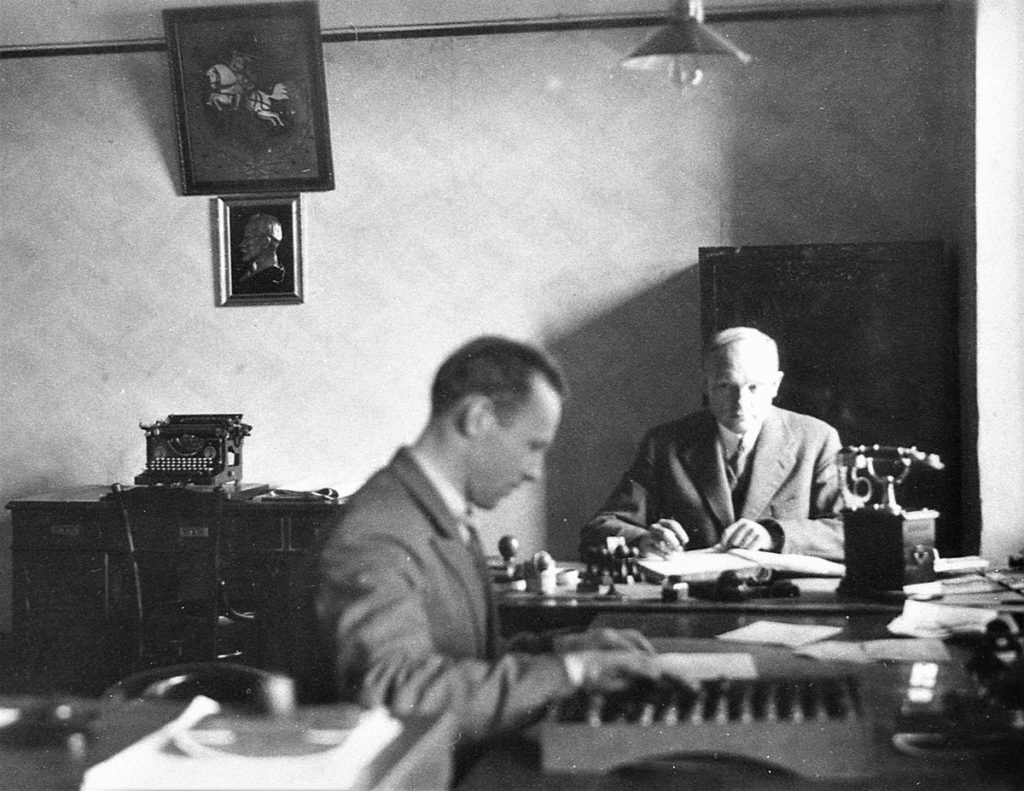 Lietuvos ūkio banko Kretingos skyriaus vedėjas Simonas Jurgis Simutis (antrame plane) už darbo stalo. Simono J. Simučio nuotr. 1931 m. Iš Kretingos muziejaus ikonografijos rinkinio.